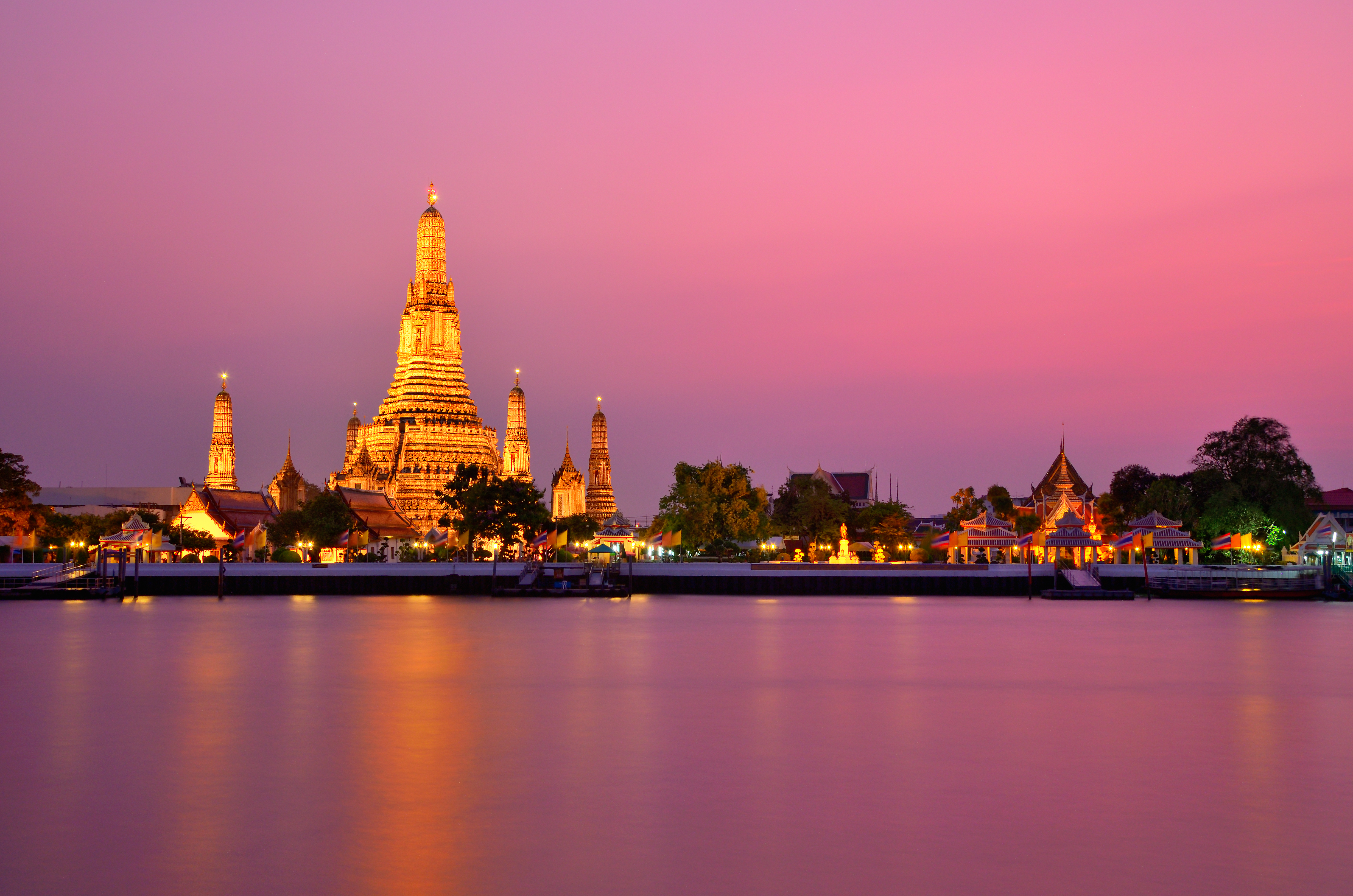 Bathed in golden light, Wat Arun sits against a pink sky at sunset in Bangkok, Thailand.