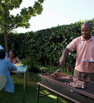 A man is braaing (Afrikaans for barbecuing or roasting) in the garden for a table of guests.