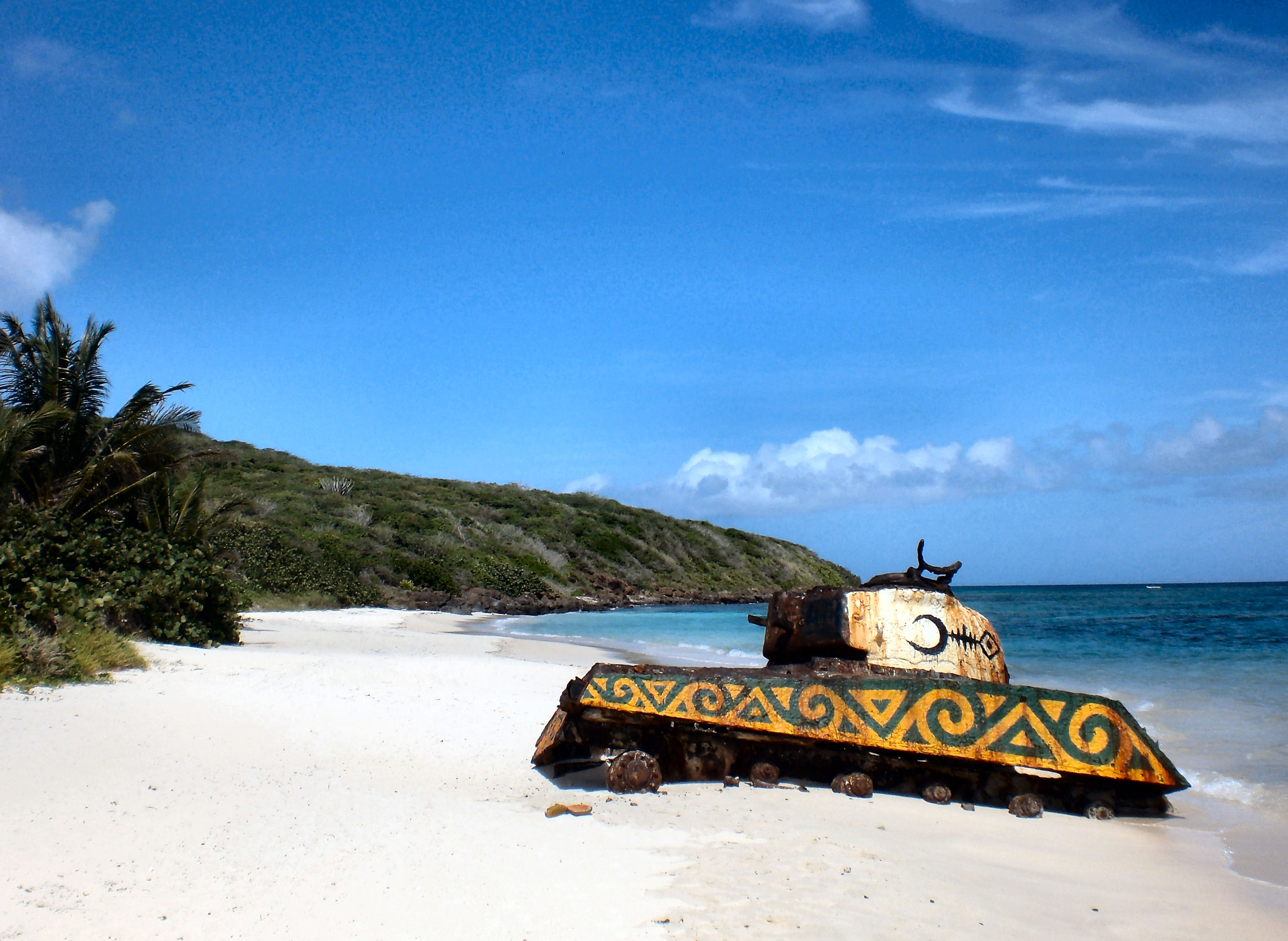 An abandoned tank on the white sands of Flamingo Beach, Pureto Rico which has been painted in yellow and green by a local artist