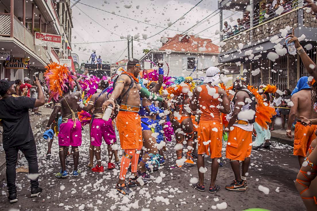 A group of people dressed in bright orange and hot pink play in foam during Carnival in Dominica