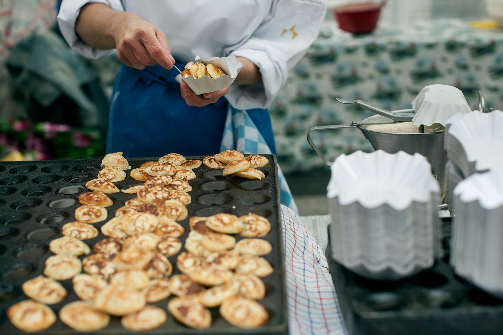 A chef places small pancakes into a cardboard tray at a street market