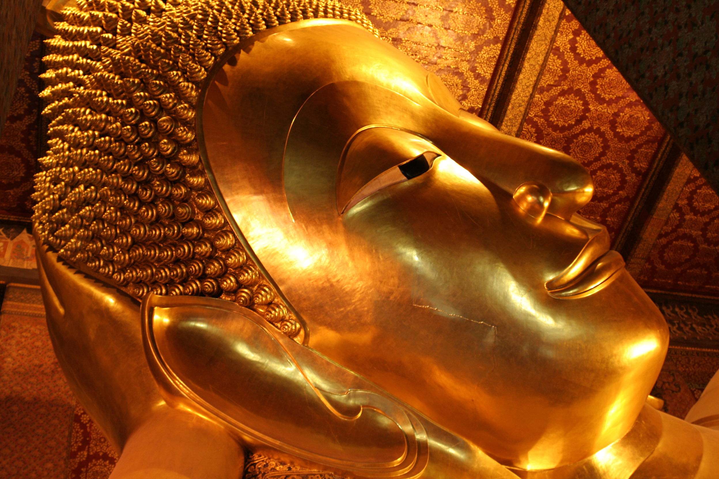 The smiling face of the massive Reclining Buddha in Bangkok in gold leaf