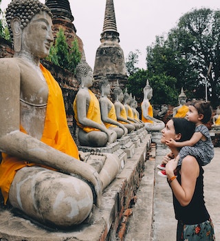 Ayutthaya, Buddha statues in a row in Wat Yai Chai Mongkhon, mother and daughter in front of a Buddha statue.