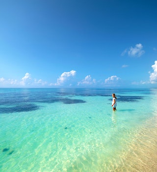 A girl stands in the shallow water of a turquoise ocean