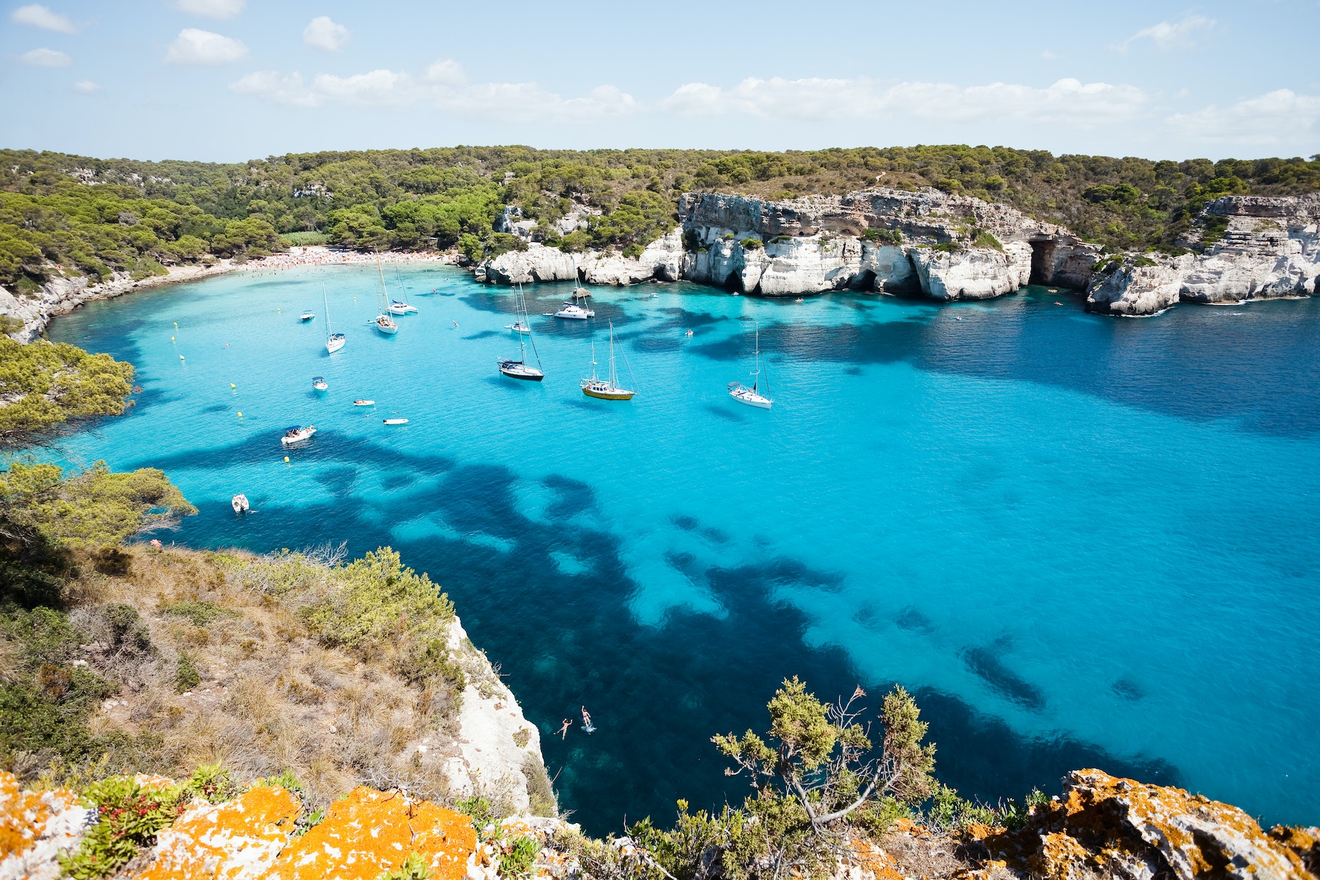 Boats sit in a deep blue coastline in Spain. 