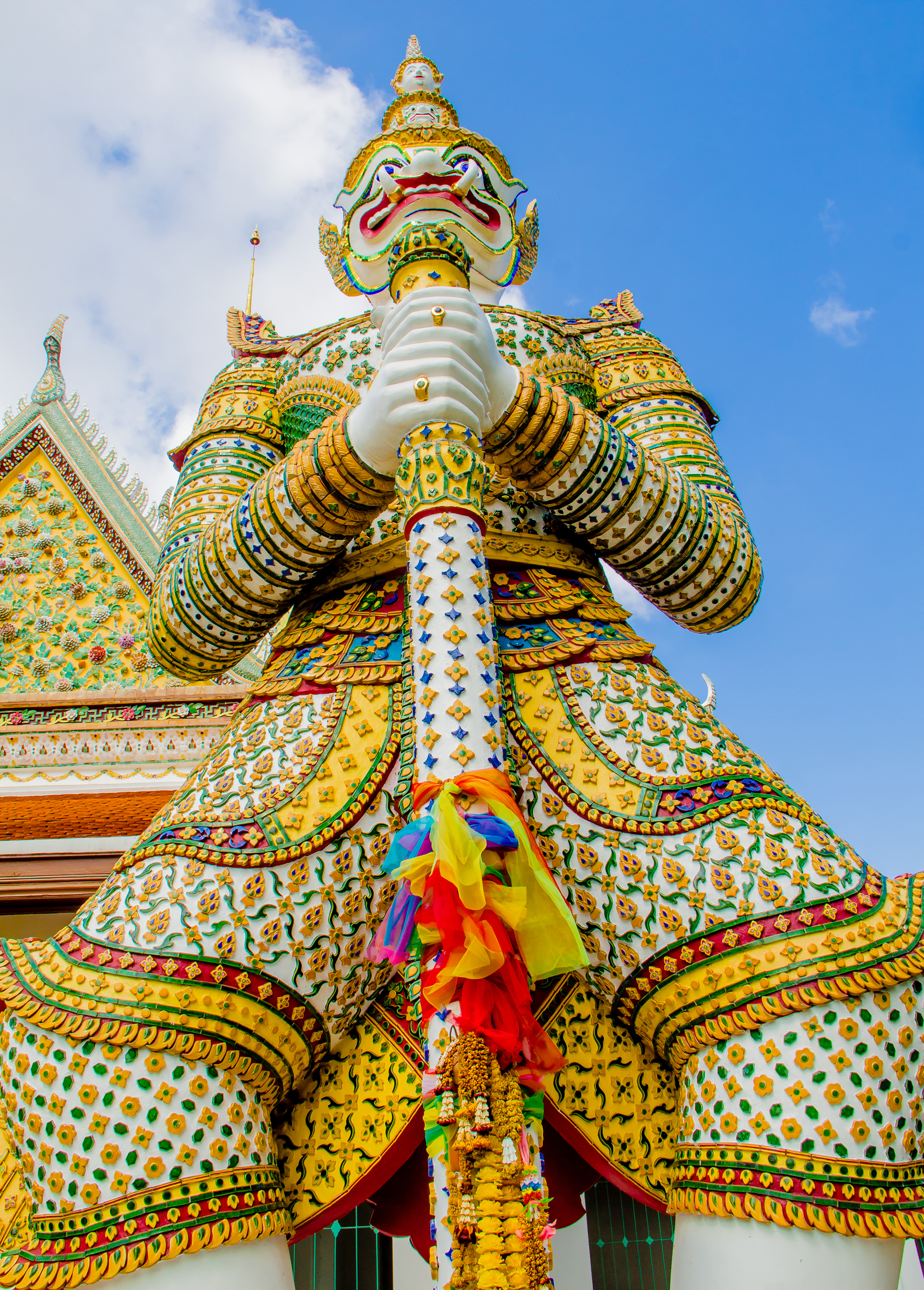 A colorful dvarapala (gate guardian) statue at the Grand Palace in Bangkok with a fearsome face and Thai headdress holding a baton.
