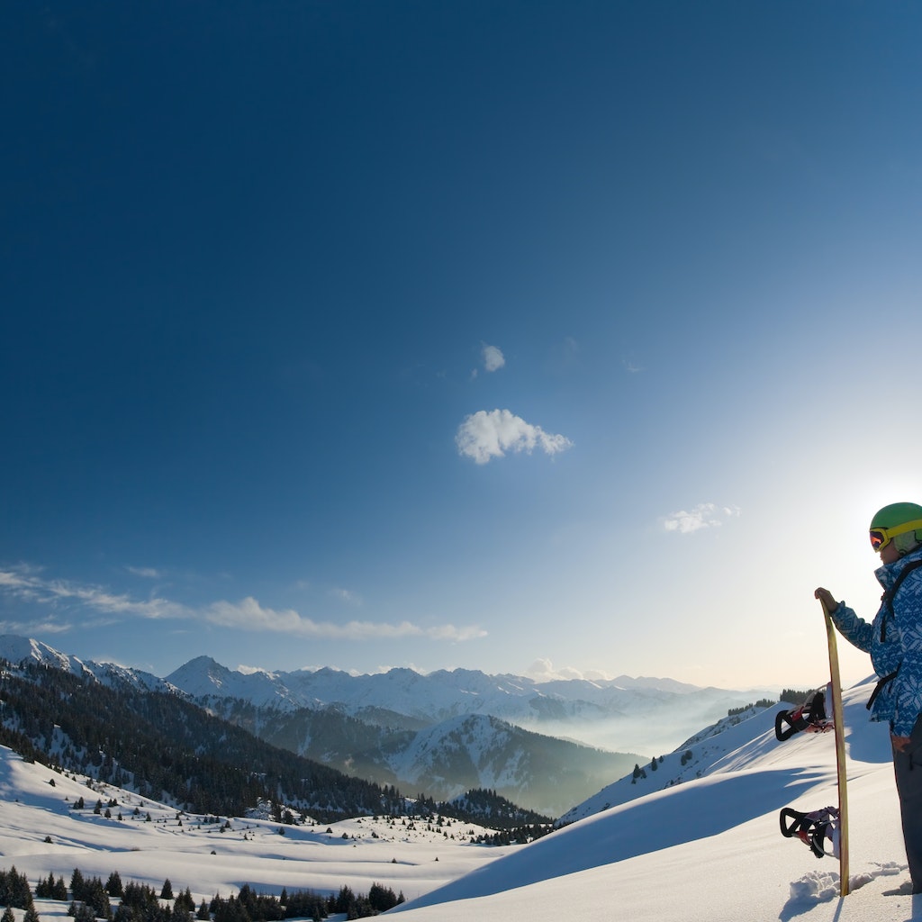 An image with a portrait of a female snowboarder wearing a helmet with a bright reflection in the glasses on the background of high snow-capped Alps in Grindelwald, Swiss